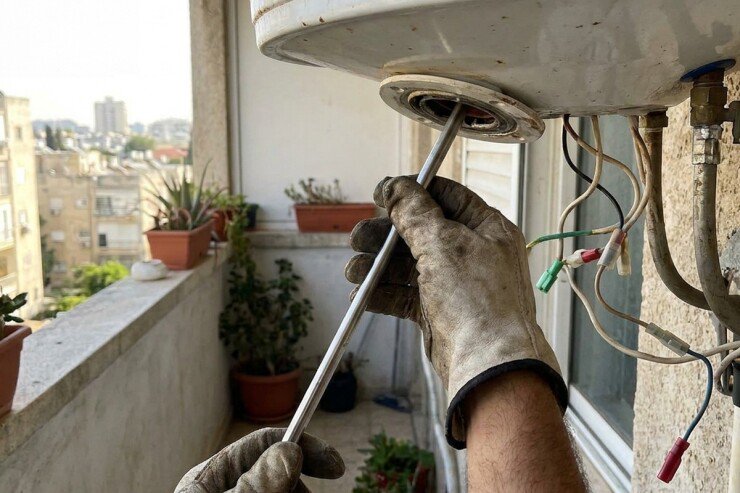 טכנאי דודים מכניס תרמוסטט חדש לשרוול שבתחתית דוד החשמל